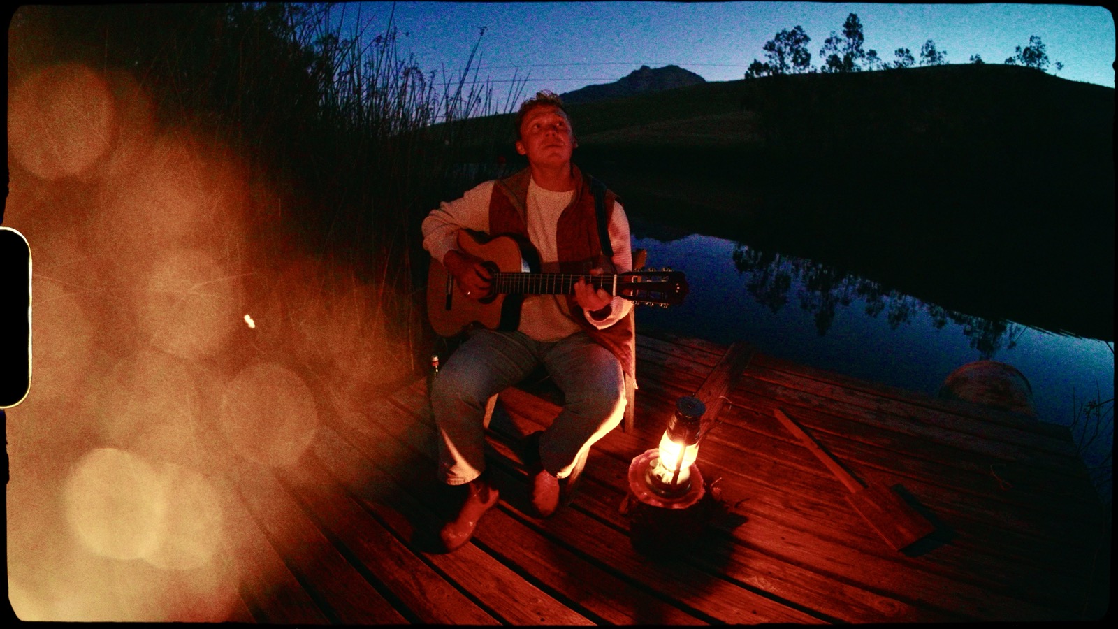 Shawn Chasten playing guitar by the water at dusk