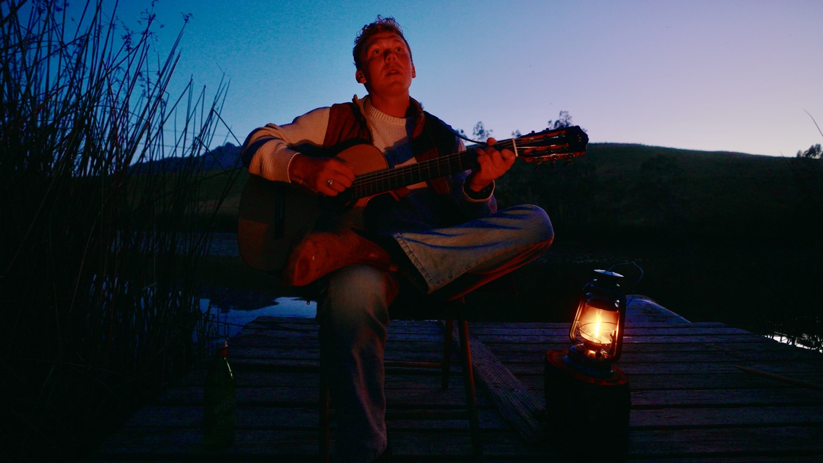 Shawn Chasten playing guitar by lantern light at dusk